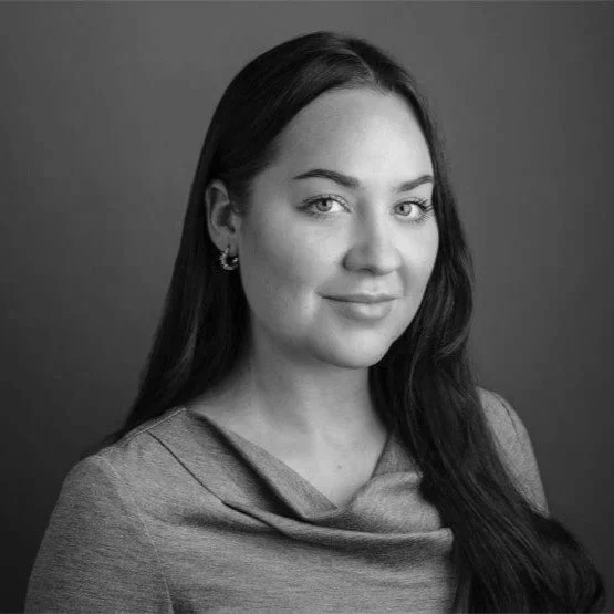 Black and white portrait of a young woman with long dark hair, smiling slightly, wearing earrings and a top with a cowl neckline.