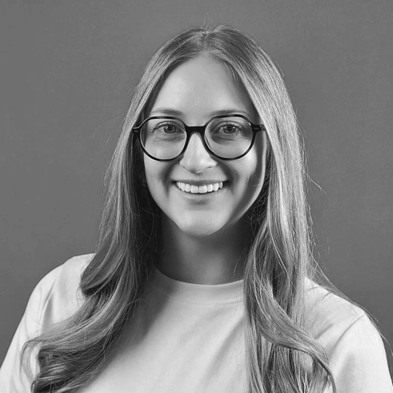 A young woman with long hair, glasses, and a friendly smile, wearing a light-colored shirt against a plain background.