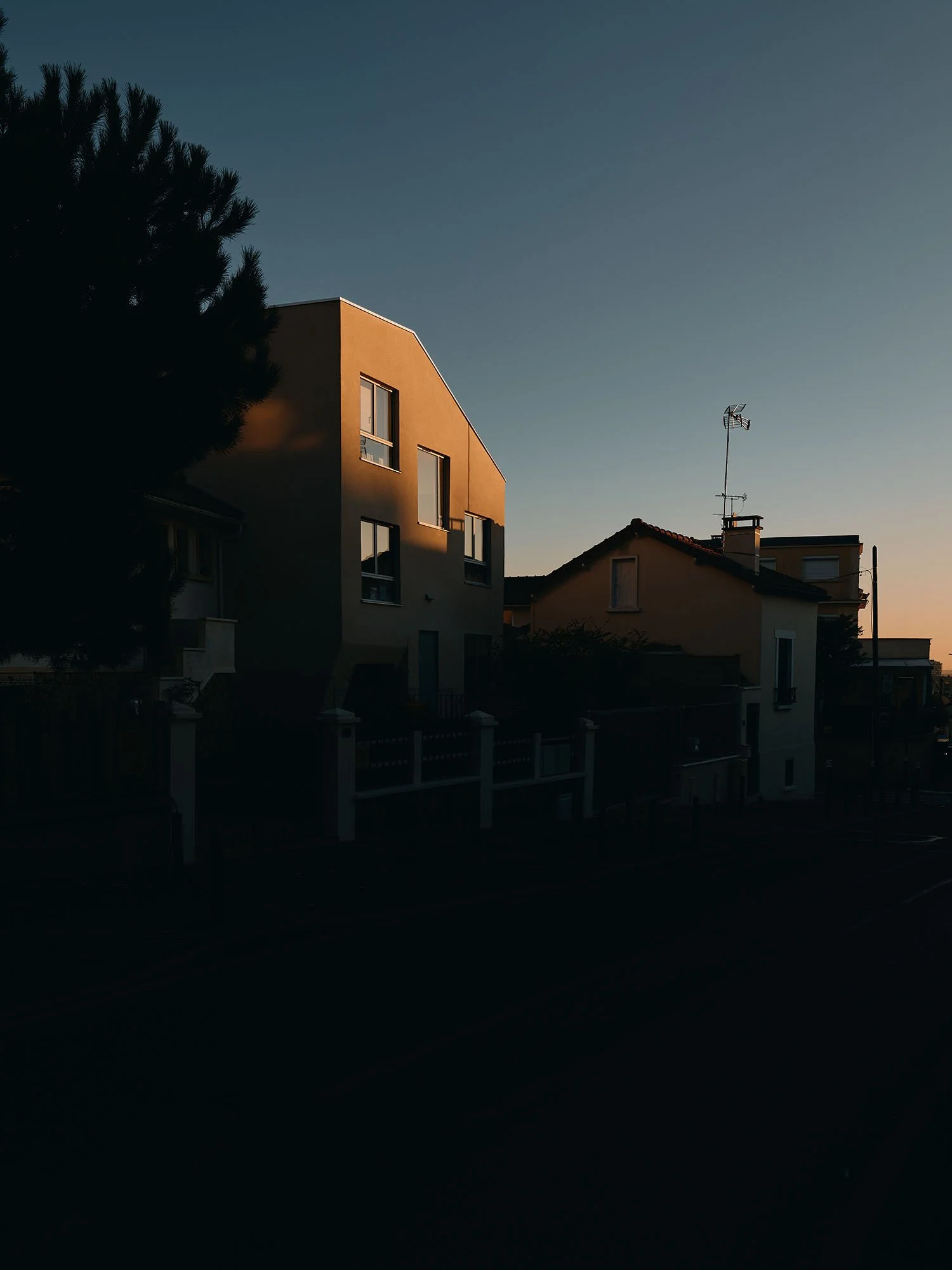 Sunset over a residential neighborhood with houses and trees, with sunlight casting shadows on the buildings.