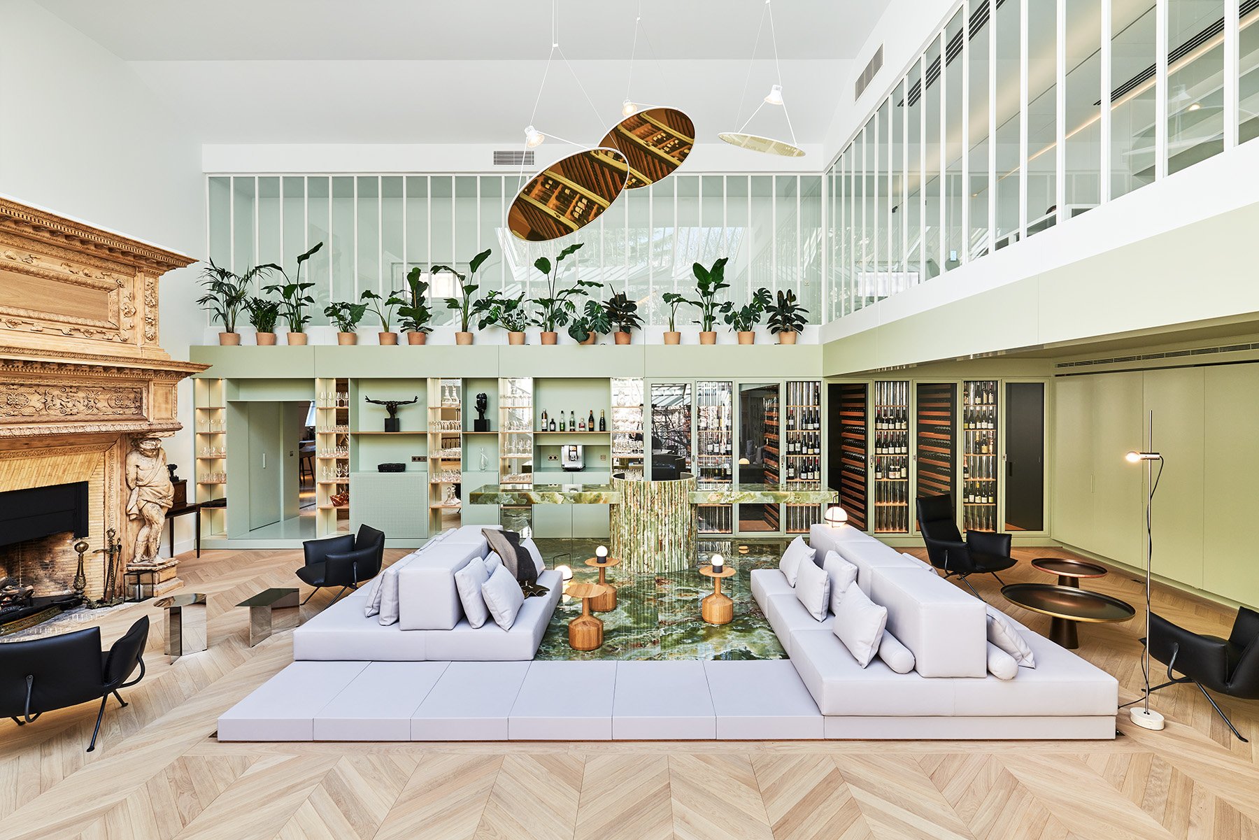 Modern living room with white sofas, black chairs, wooden tables, a fireplace, and decorative plants on an upper shelf.