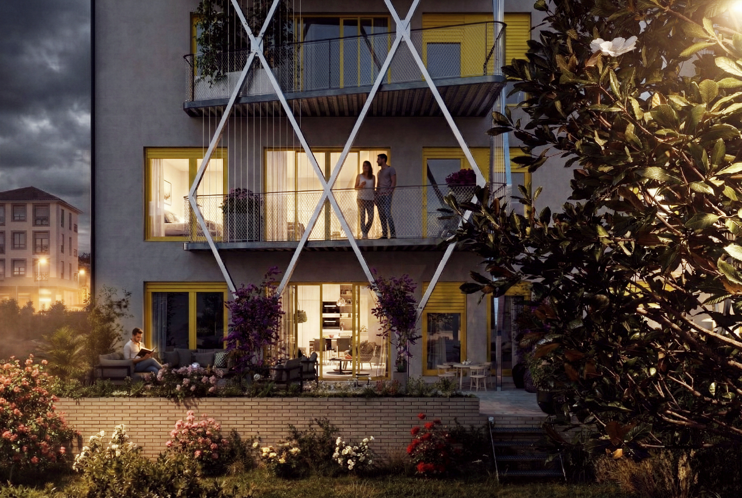 Edificio moderno de varios pisos con balcones y ventanas con marcos amarillos, rodeado de jardines y flores, en la noche con luces encendidas y un cielo nublado.