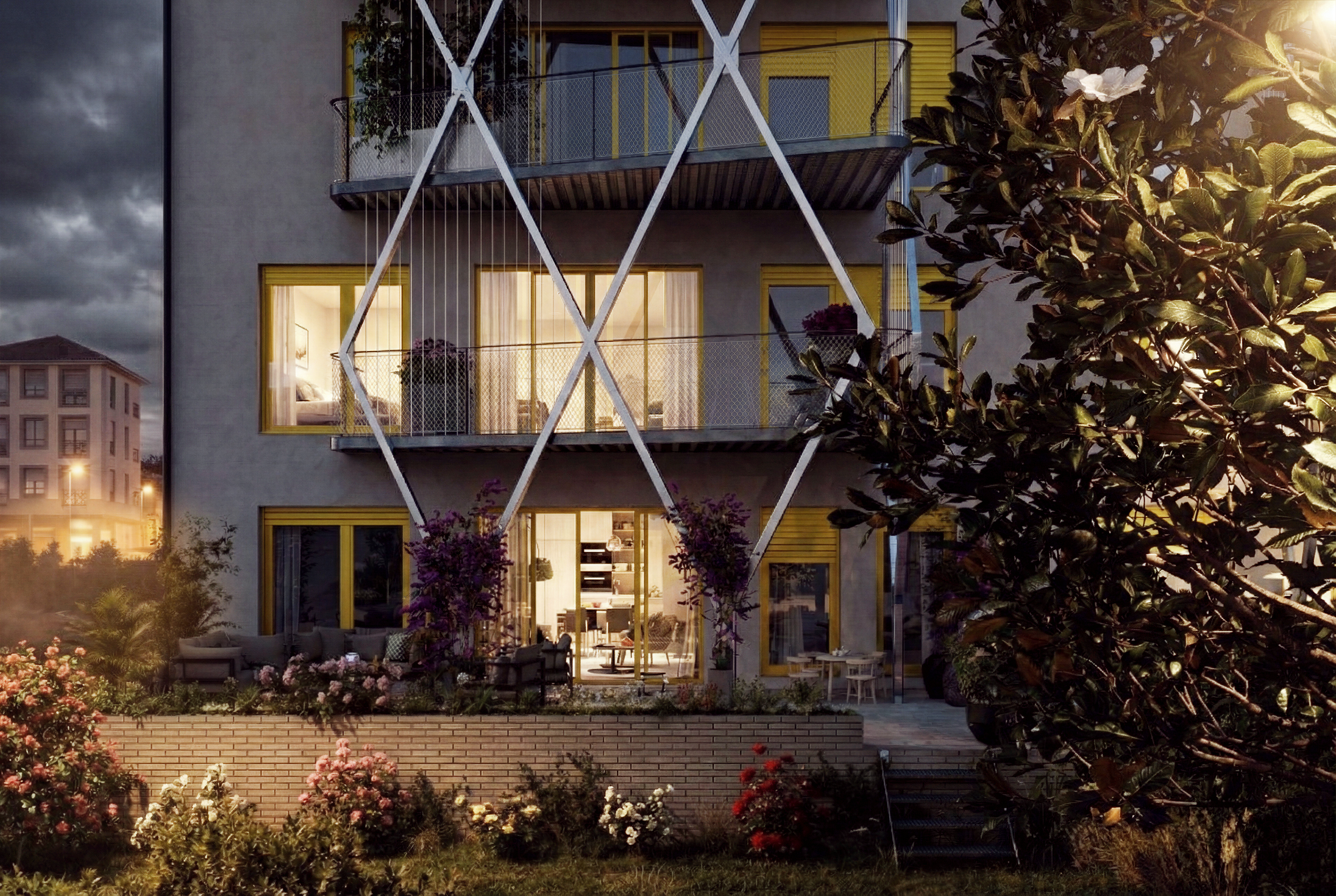 Edificio moderno de varios pisos con balcones y paredes amarillas, rodeado de un jardín con flores y árboles, en la noche con luces encendidas en el interior.
