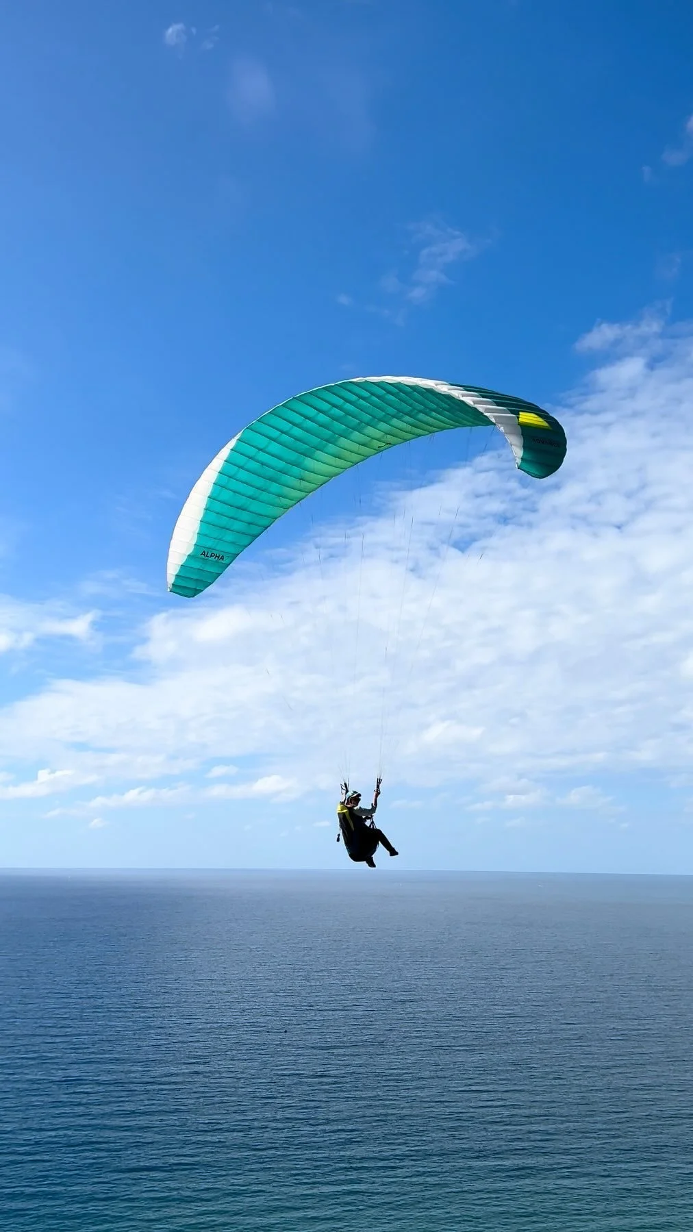 A person paragliding over the ocean with a blue sky and clouds in the background.