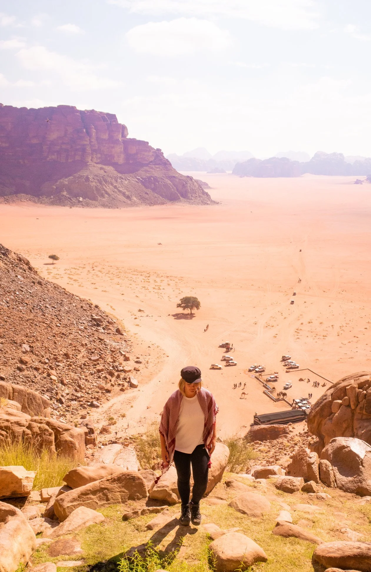 A woman hikes up a rocky hill with a desert landscape and mountains in the background.