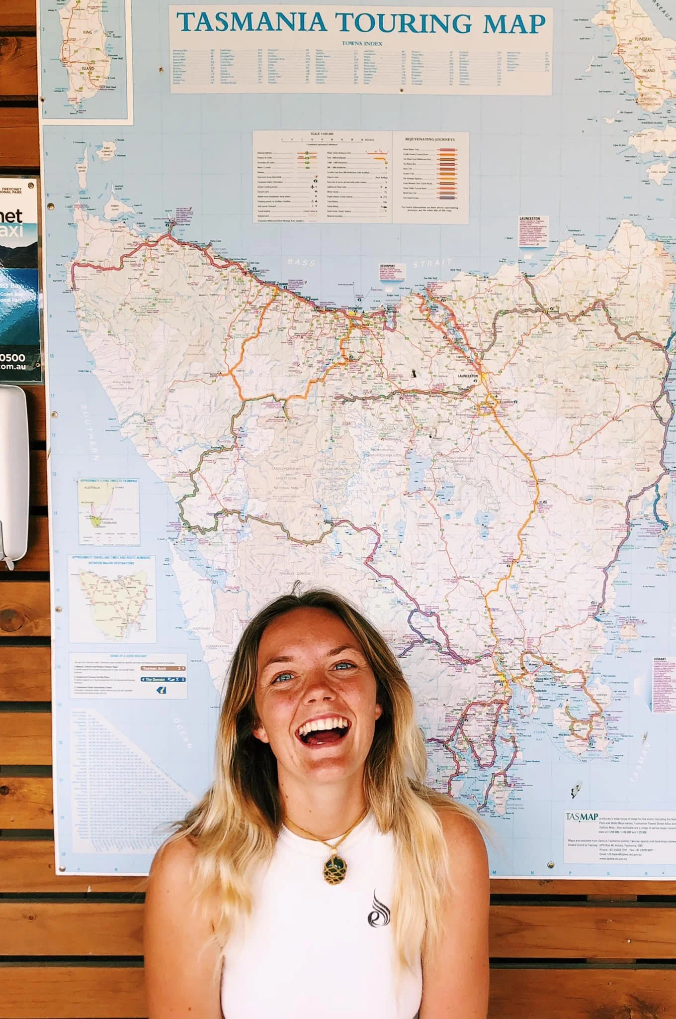 A woman with blonde hair, smiling and laughing, standing in front of a large map of Tasmania.