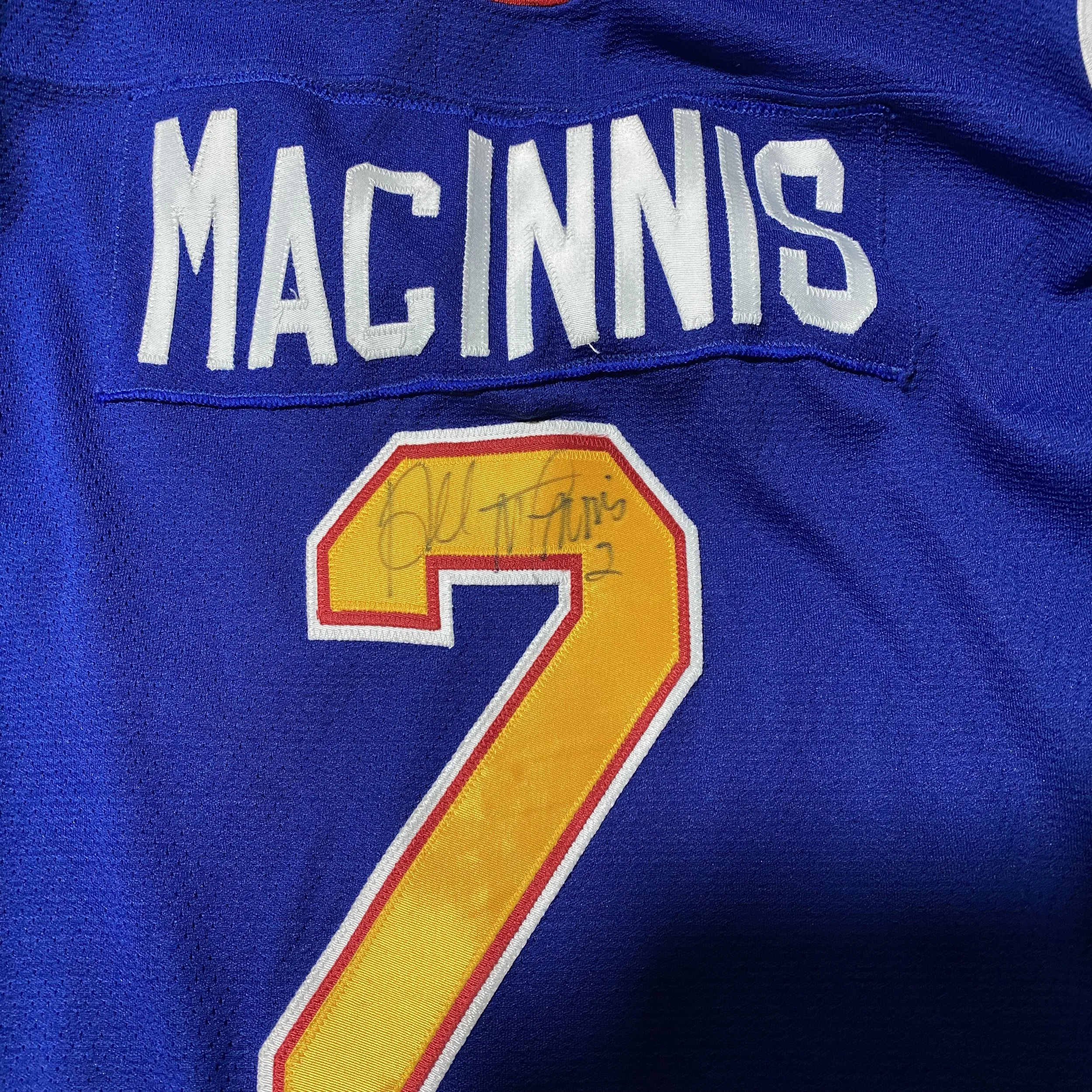 Close-up of a sports jersey with the name 'MACKINNS' above the number 2, which is yellow with a red and white border. There is an autograph on the yellow part of the number.