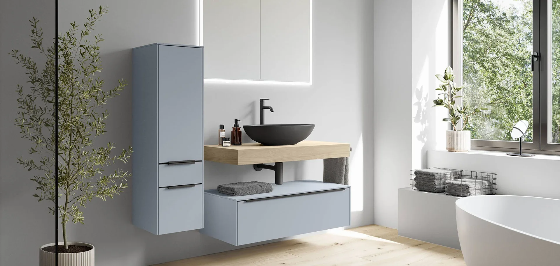 Modern bathroom with a black vessel sink on a wooden vanity, a large window with greenery outside, a potted plant on the windowsill, and a white bathtub. There's also a light blue cabinet, gray towels, and minimal decor.