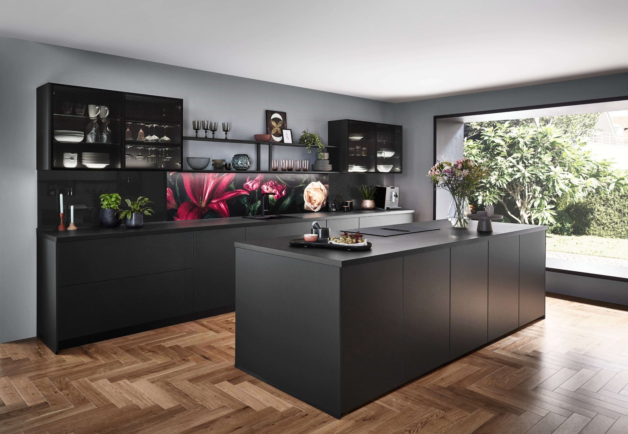 Modern kitchen with dark cabinets, floral backsplash, and large window overlooking greenery.