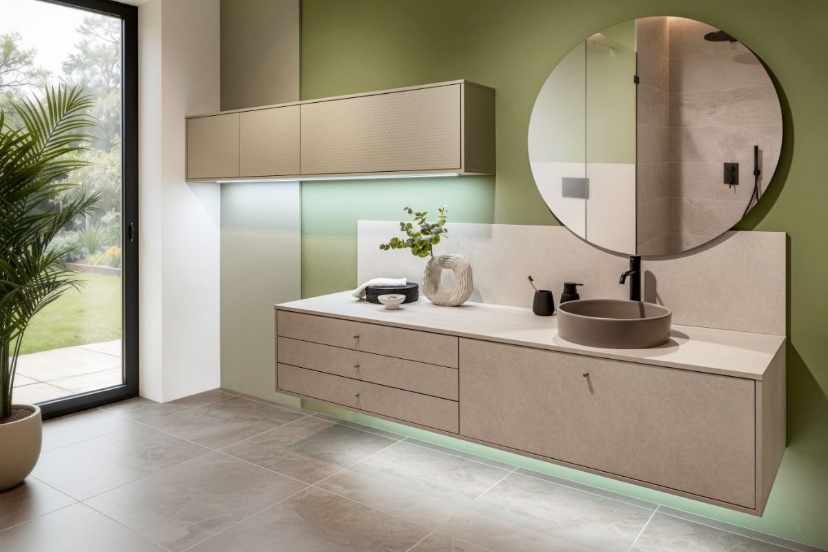 Modern bathroom with floating vanity, round mirror, basin sink, and natural light from a glass door leading to a garden.