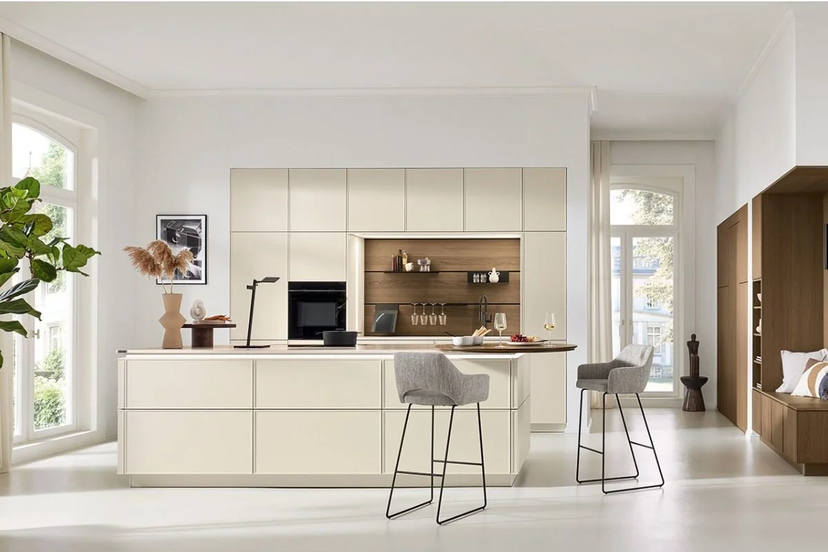 Modern white kitchen with a center island, bar stools, open shelves, and large windows letting in natural light.