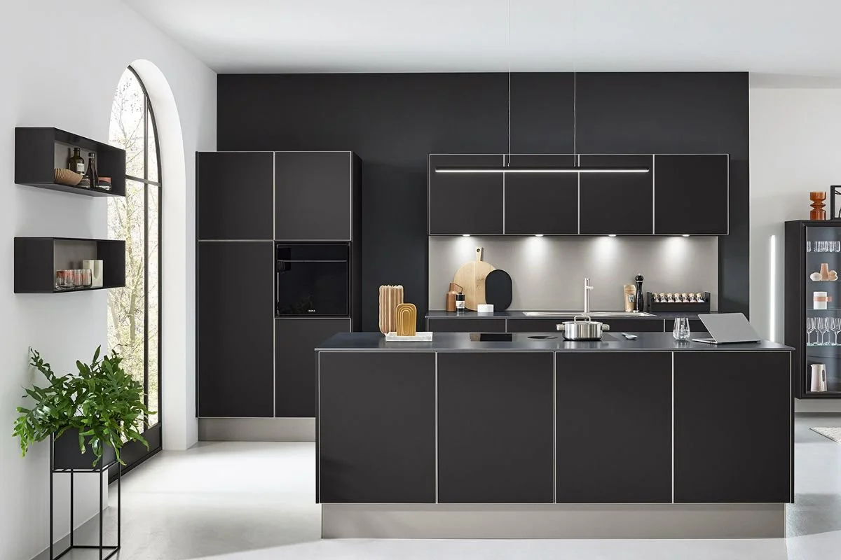 Modern black kitchen with minimalist design, black cabinets, and a black kitchen island, complemented by a white countertop and a large arched window.