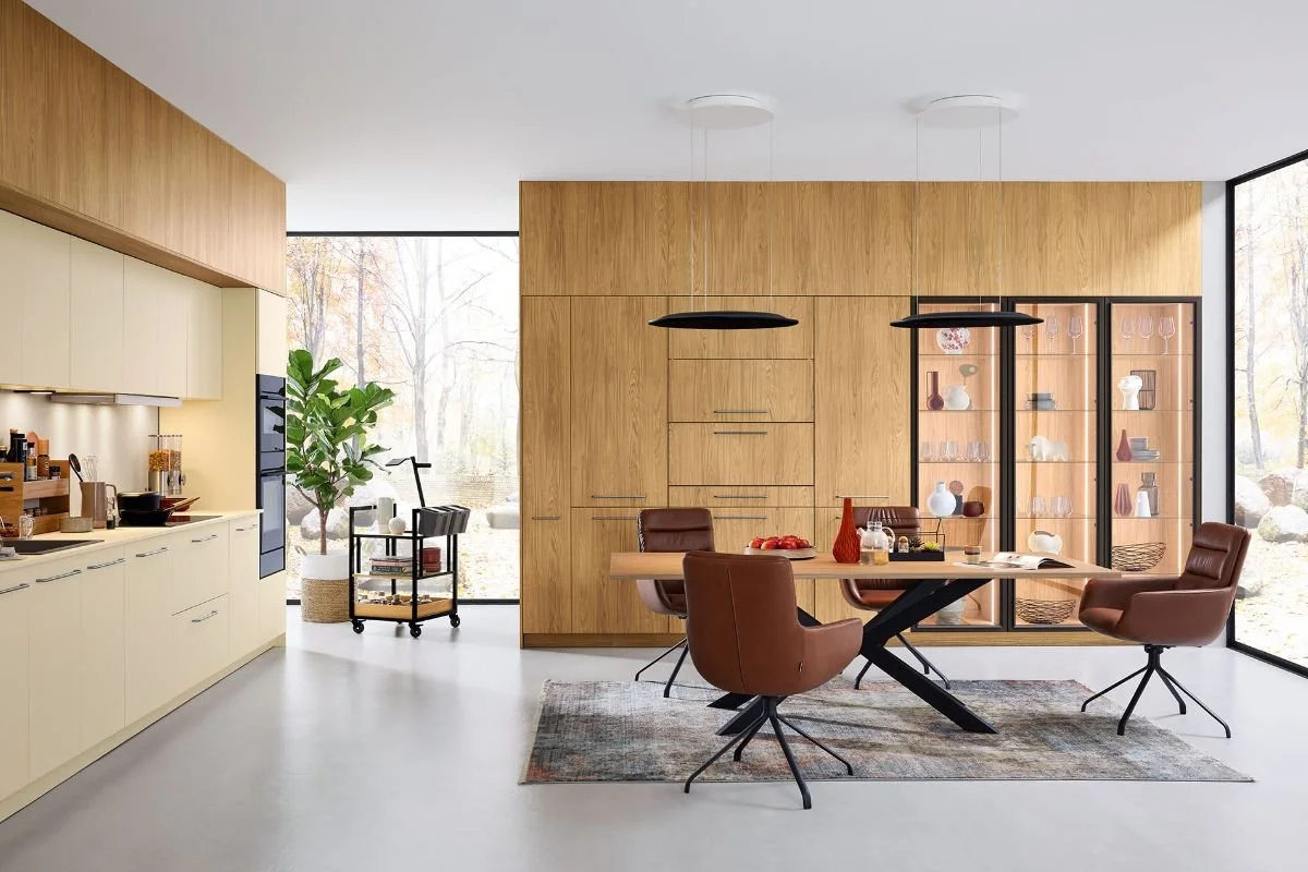 Modern dining area with a wooden table, four brown chairs, a glass display cabinet with decorative items, and large windows showing outdoor scenery.