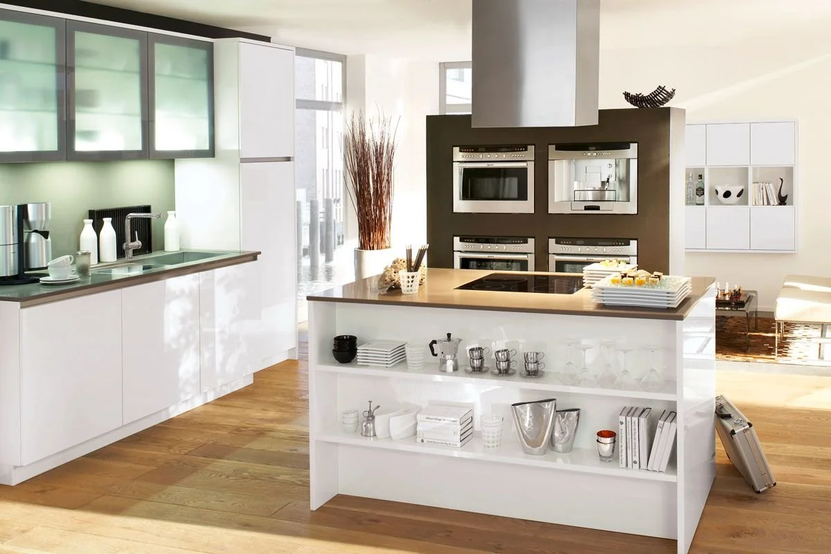 Modern kitchen with white cabinets, a central island, built-in ovens, and open shelves with various kitchen items.