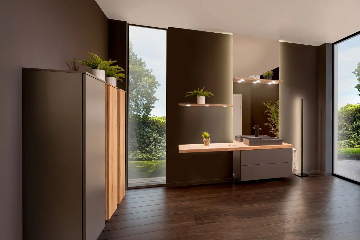 Modern bathroom with dark walls, large windows showing green trees outside, a floating vanity with a sink, plants for decoration, and wooden cabinets.