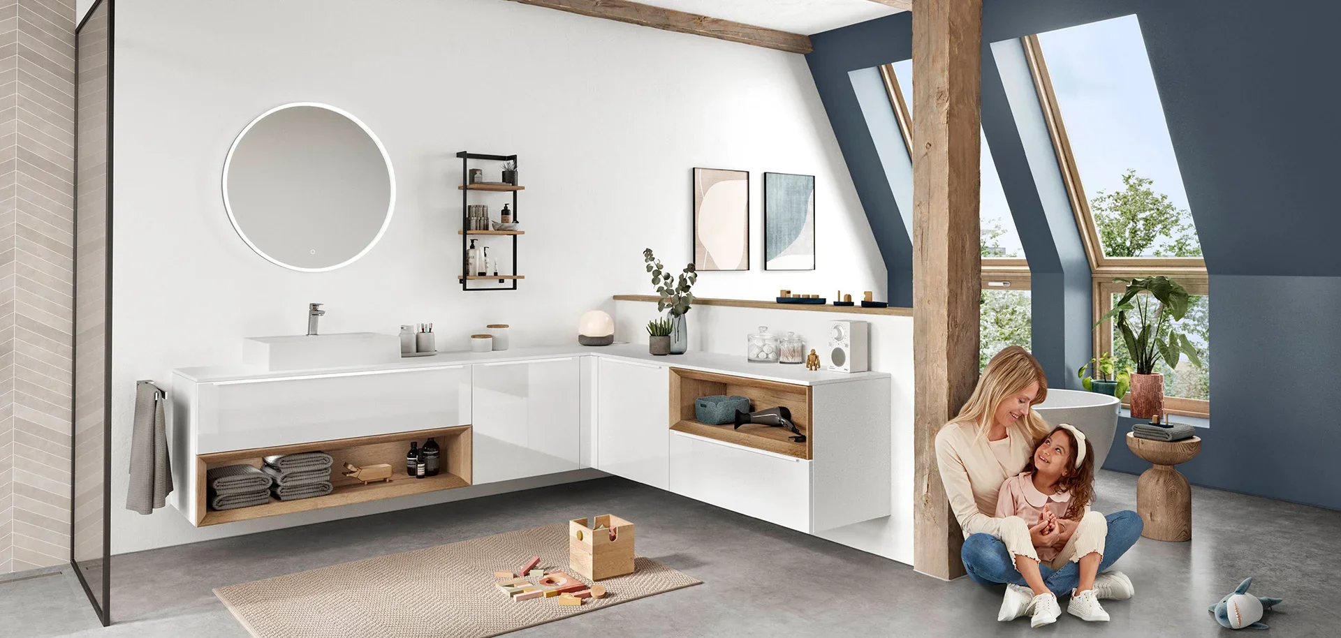 A modern bathroom with white and wooden accents, featuring a vanity with a round mirror, a woman and a child sitting on the floor near a blue wall with large windows, and various plants and decor.