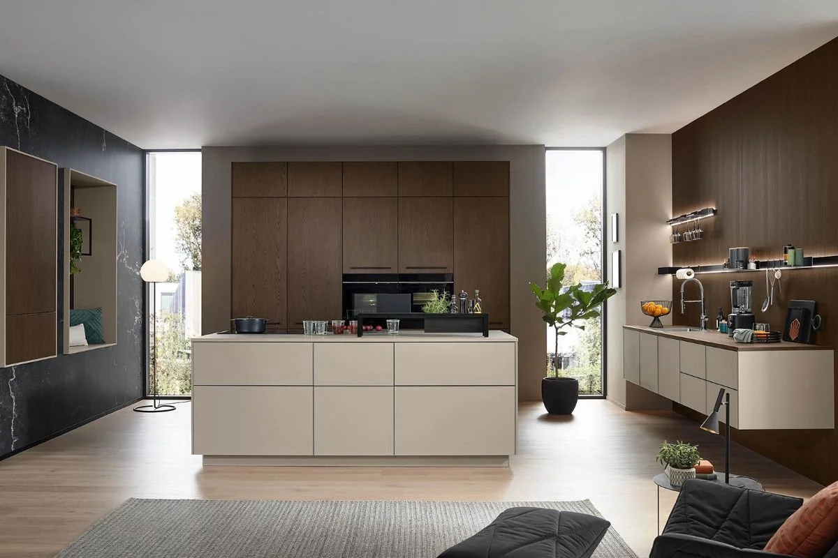 Modern open-concept kitchen with white island, wooden cabinetry, and black accents, adjacent to a living area with a gray sofa and a small side table.