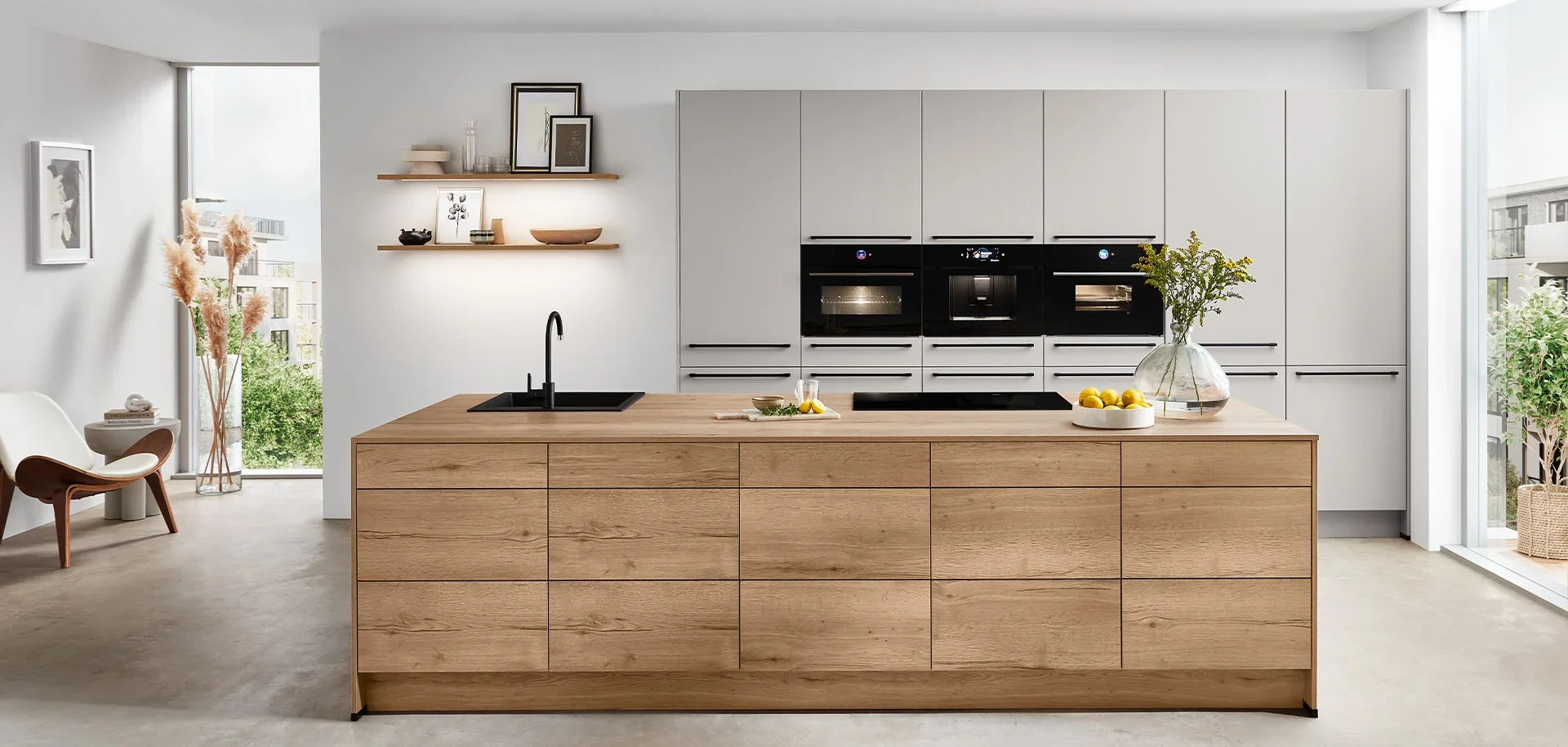Modern kitchen with wooden island, white cabinetry, black appliances, and large windows with natural light.