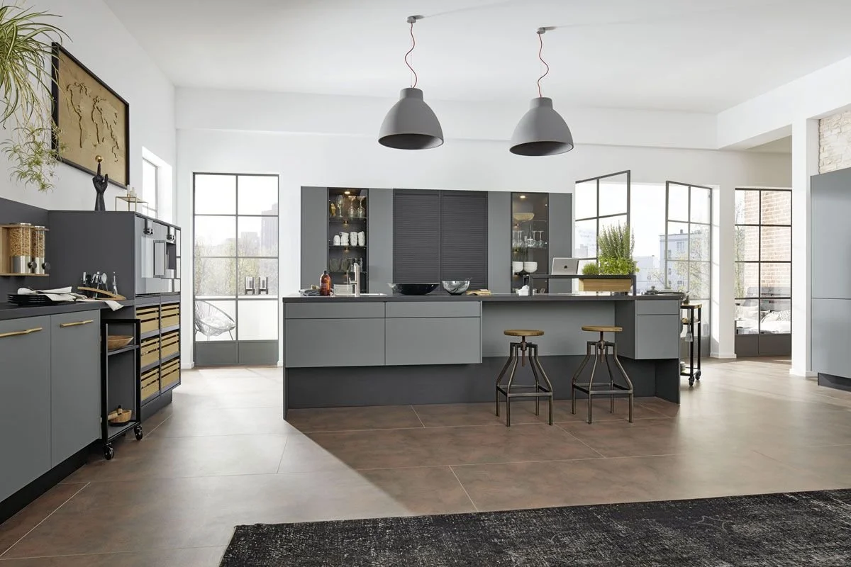 Modern open-concept kitchen with gray cabinets, large central island, black stools, pendant lights, and large windows letting in natural light.