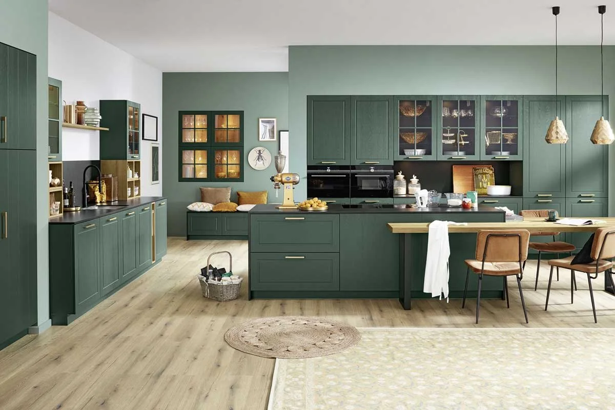 Modern kitchen with green cabinets, wooden accents, and light wood flooring, featuring a kitchen island, seating area, and decorative items.