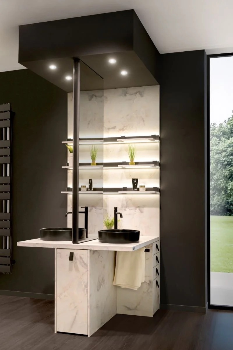 A modern bathroom with a marble vanity, black sinks, and black faucets. Shelves with small plants and toiletries are illuminated with LED lighting. Large window with a view of greenery outside.