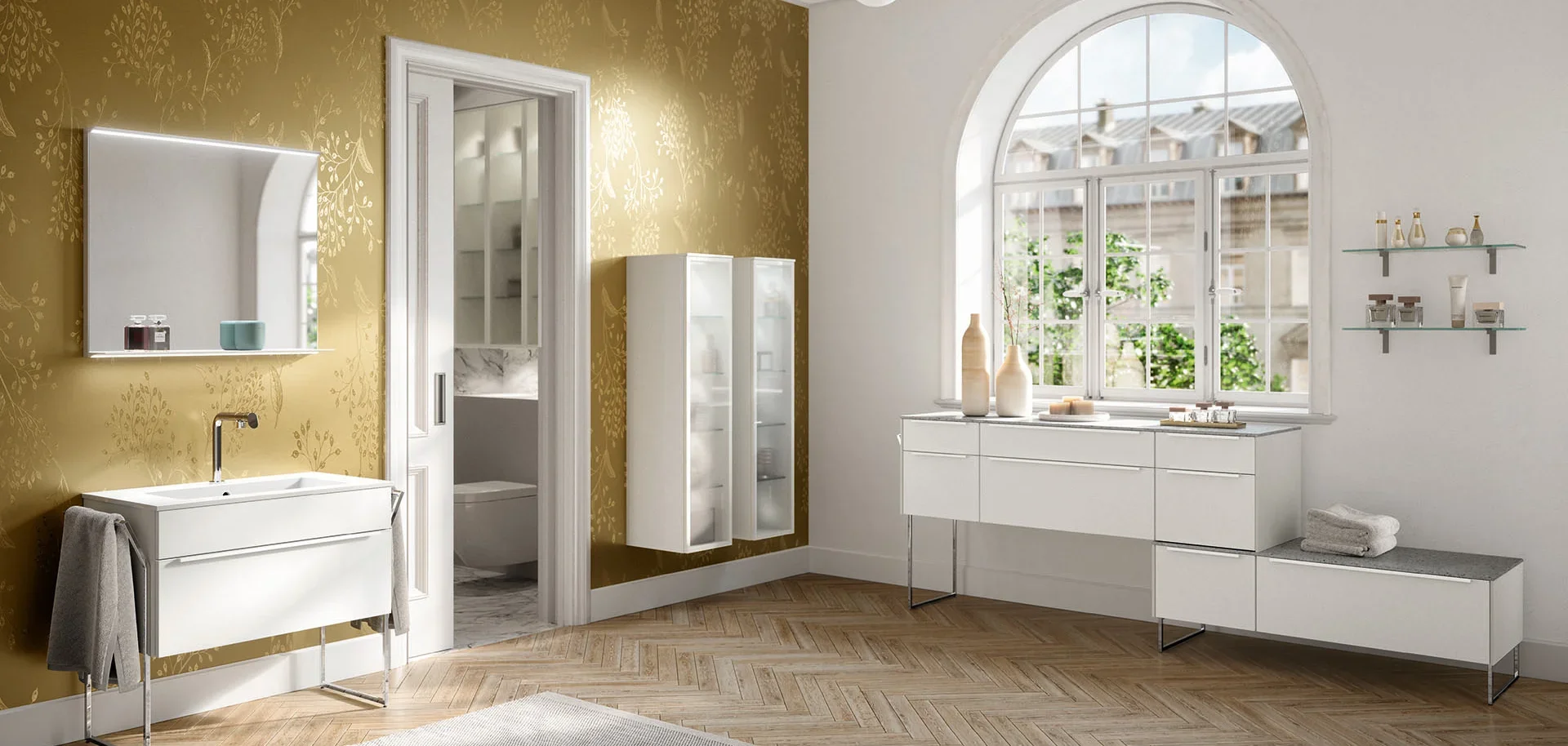 Bright, modern bathroom with gold floral wallpaper on the left wall, white vanity with a mirror above, a glass cabinet, and a large arched window showing outdoor buildings and greenery.