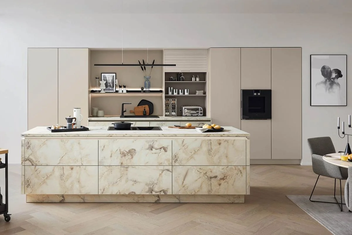Modern kitchen with marble island, beige cabinets, open shelves, black appliances, and a dining area with gray chairs.