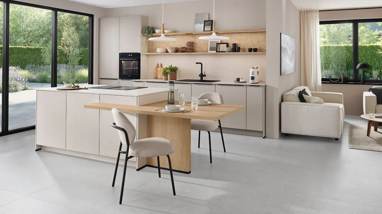 Modern open-concept kitchen and living room with large windows, white cabinets, a wooden table, and neutral-colored furniture.