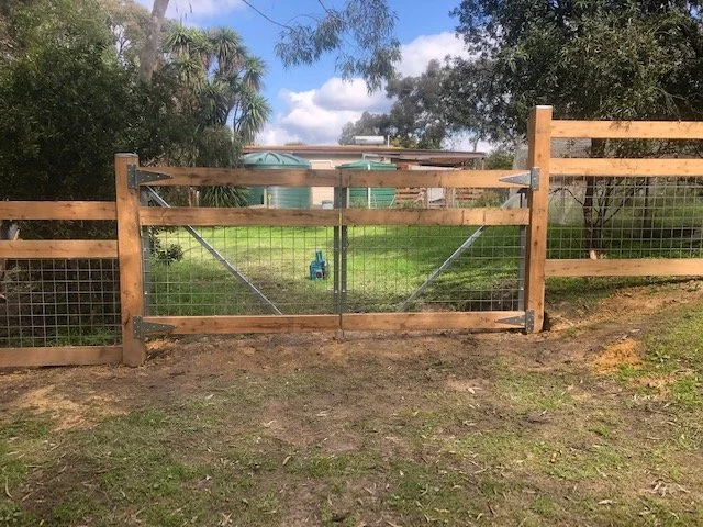 Wood and wire gate on grassy yard with trees and cloudy sky in the background.