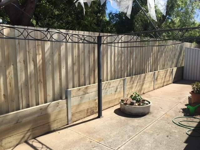 A backyard patio enclosed by a wooden fence with a planter, a garden hose, and a turned clothesline.