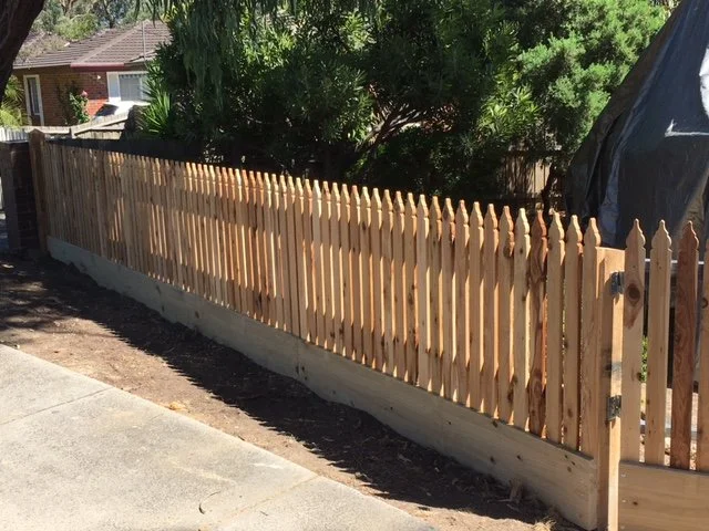 New wooden picket fence installed along a sidewalk in a backyard.