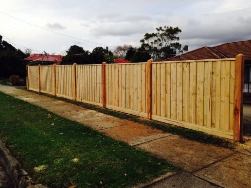 A newly installed wooden privacy fence along a sidewalk in a residential neighborhood.