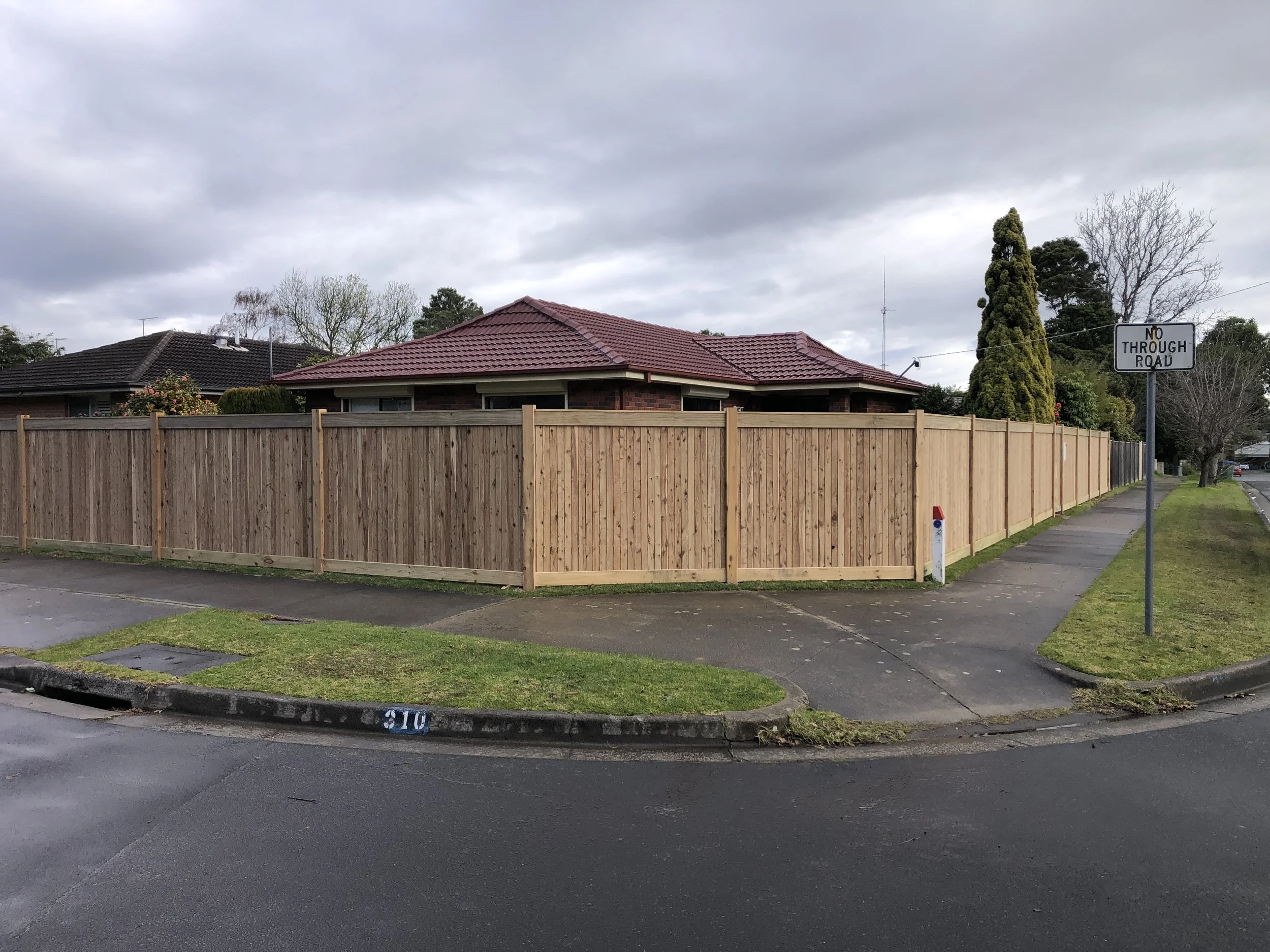 Residential house with a new wooden fence, red tiled roof, and sidewalk with a no through road sign.
