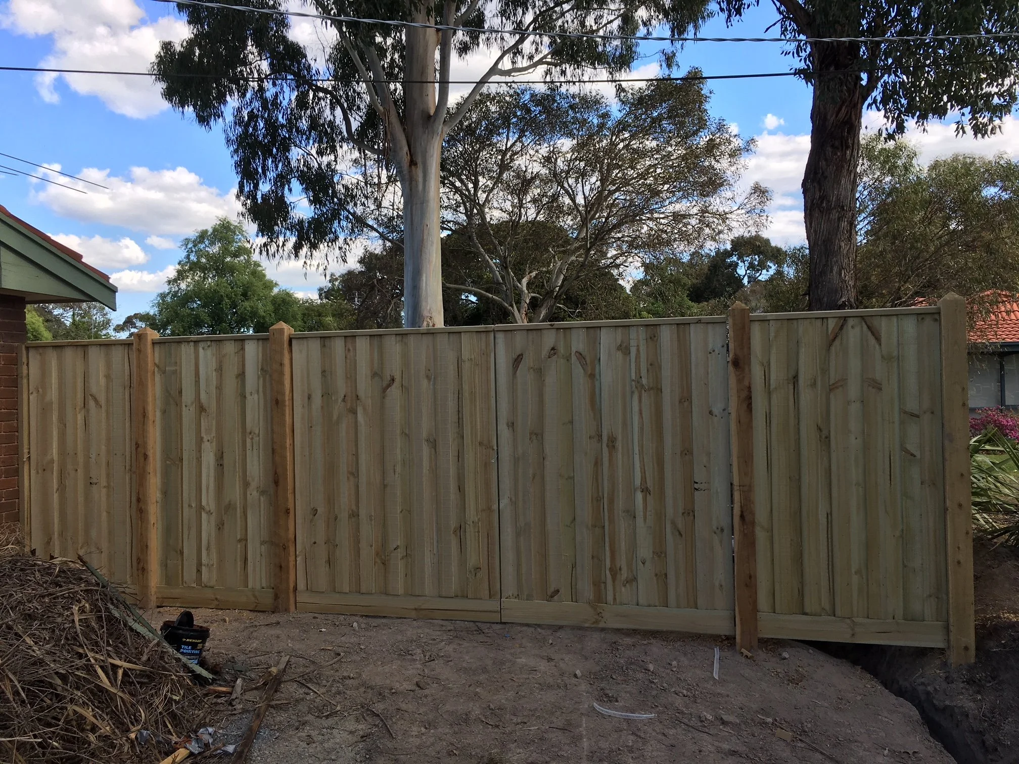 New wooden fence under construction in a backyard, with trees and a partly cloudy sky in the background.