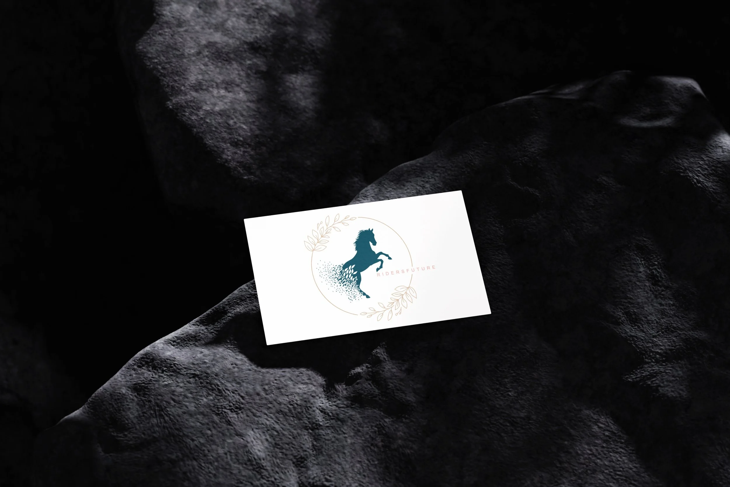 Visitenkarte mit einem Silhouette eines galoppierenden Pferdes, umgeben von Blättern, auf einem schwarzen, steinigen Hintergrund.
