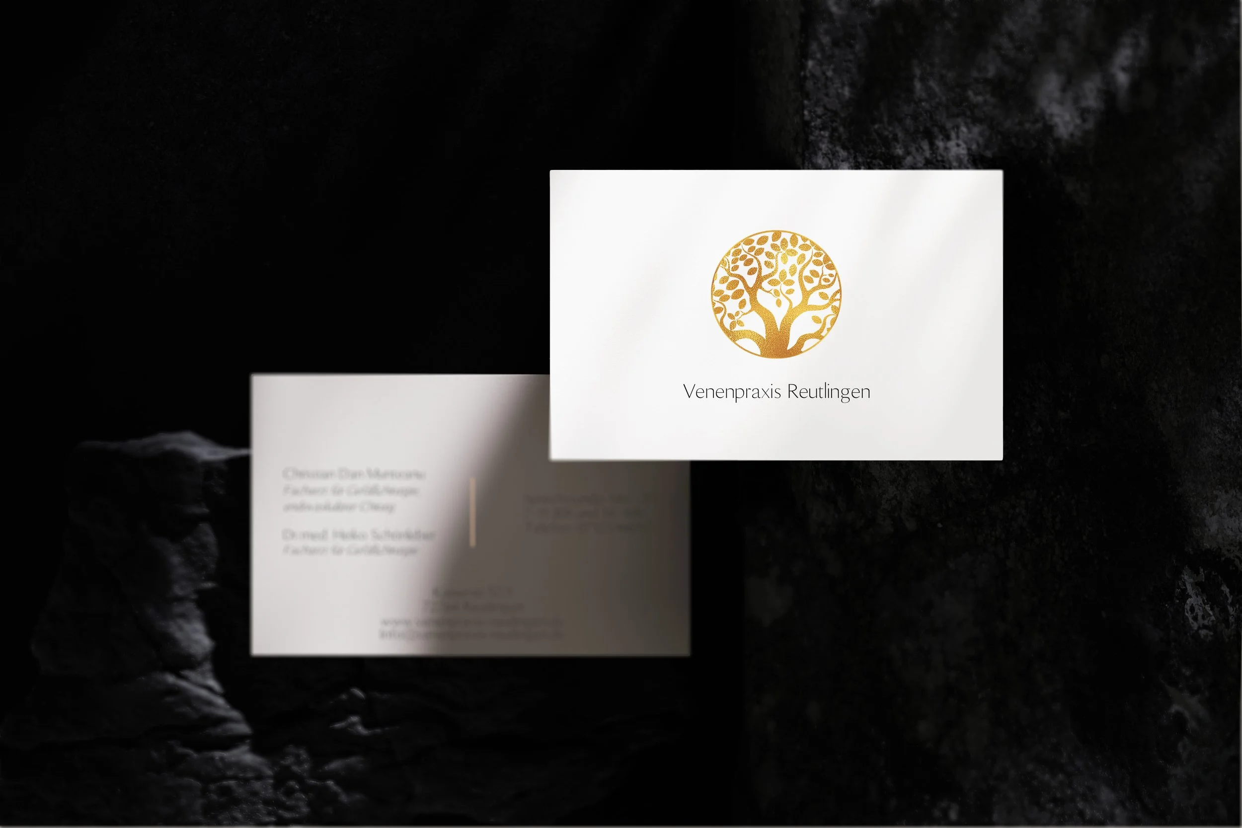 Visitenkarte mit goldenem Baum-Logo und der Textur 'Venenpraxis Reutlingen' auf weißem Hintergrund, vor einem schwarzen Gestein-Hintergrund.