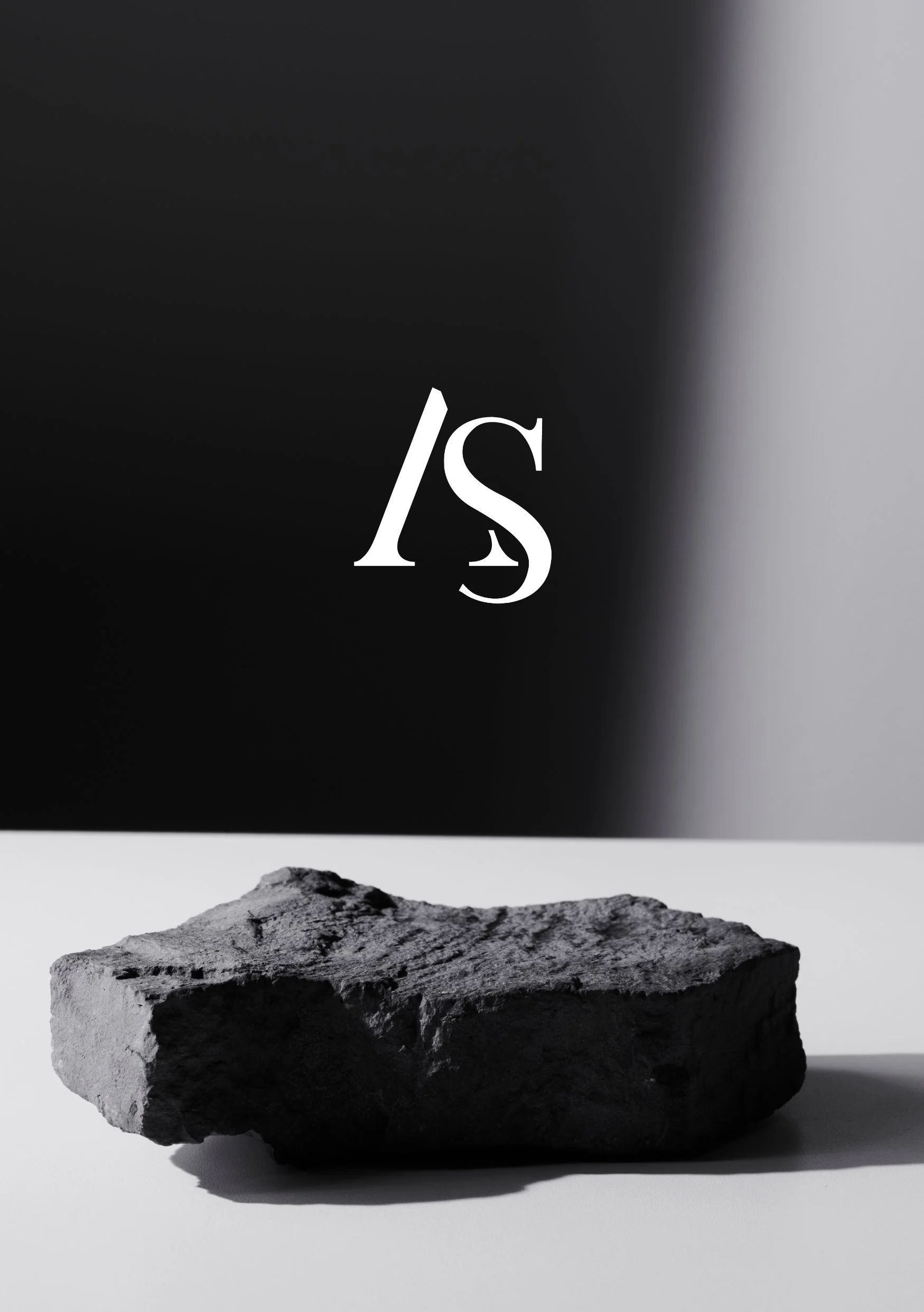 Schwarzer Stein auf weißem Tisch mit weißem Hintergrund, darüber ein schwarzer Hintergrund mit weißen Buchstaben 'IS'.