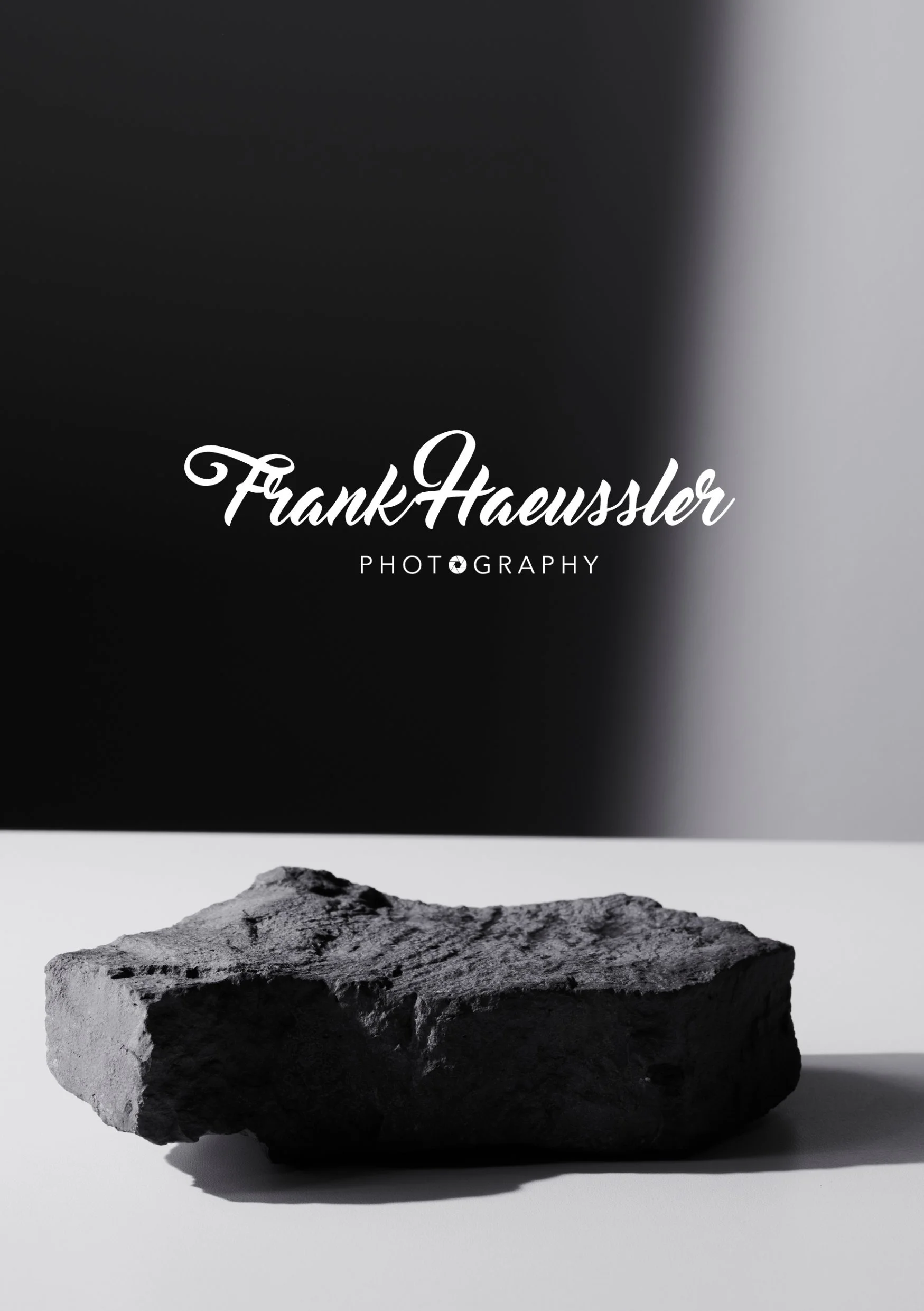 Schwarzer und grauer Hintergrund mit einem grauen Stein auf einer weißen Oberfläche, Text: "Frank Haussler Photography".