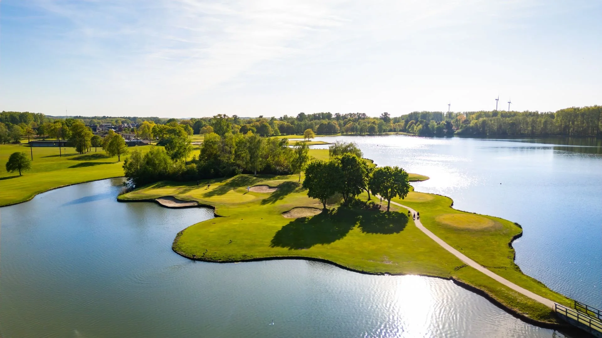 Landschap met een golfbaan en een groot wateroppervlak, omringd door bomen en grasvelden op een heldere dag.