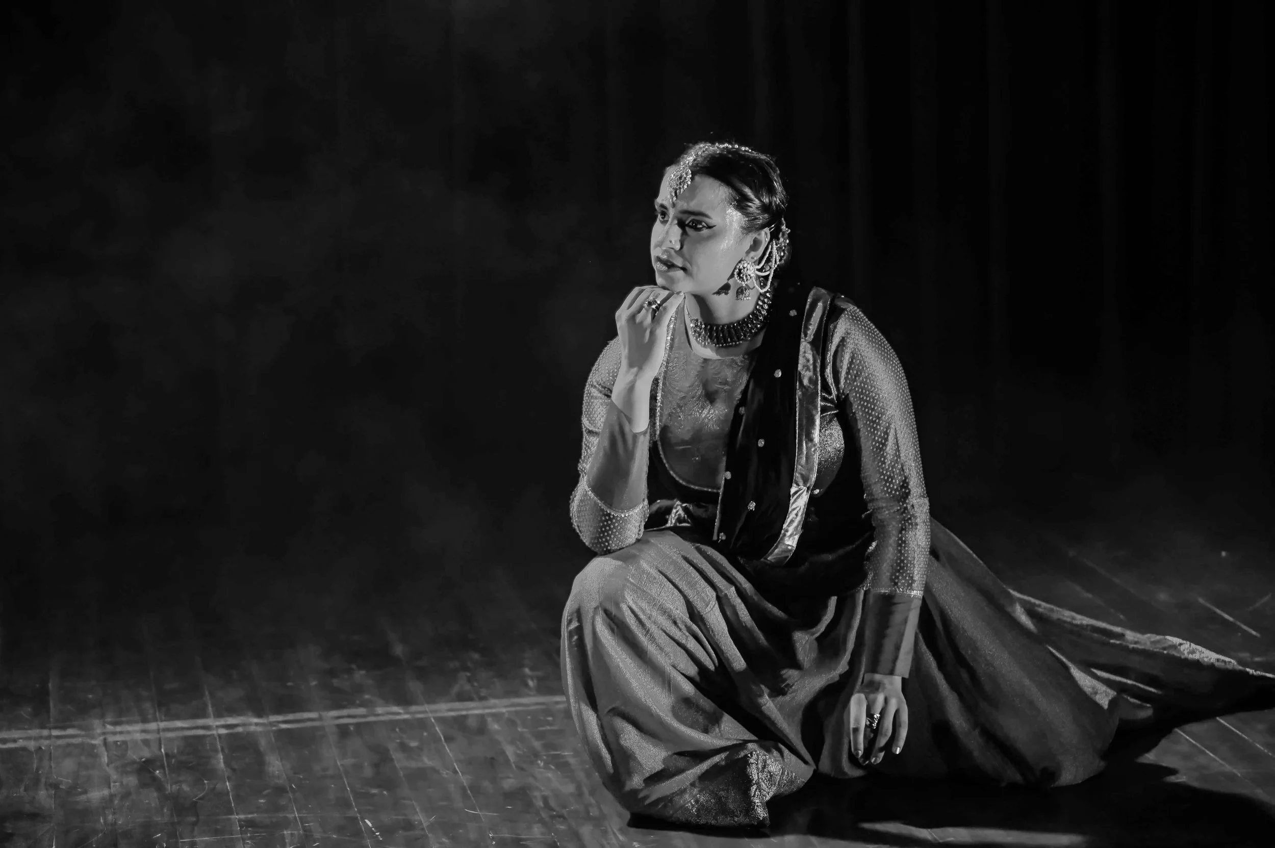 Tarini during performance, posed in concentration, looking to her left, on one knee, in black and white