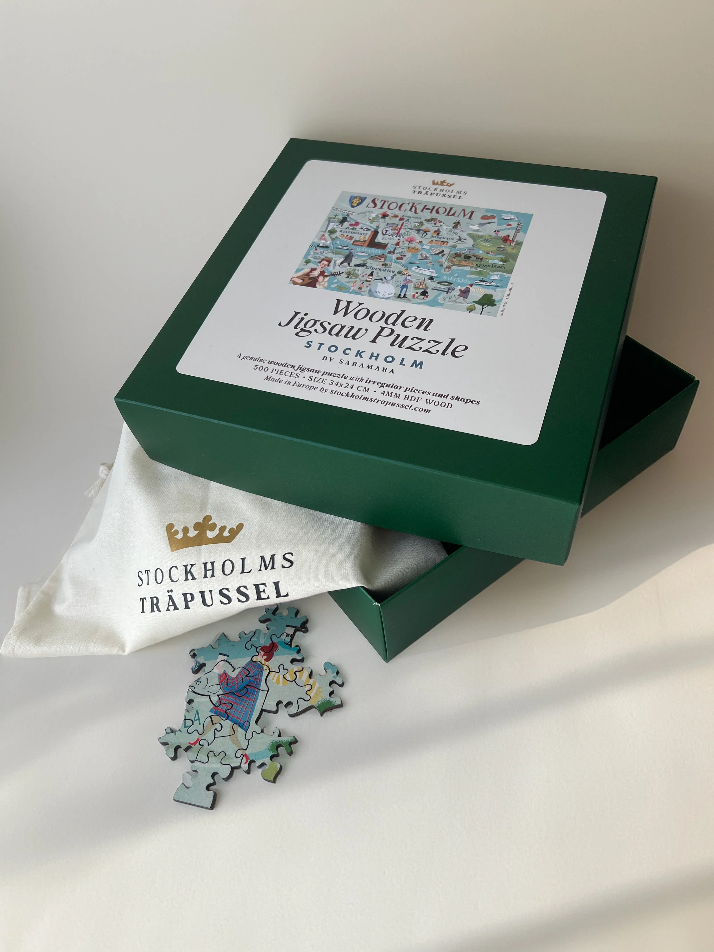 Wooden jigsaw puzzle box labeled 'Stockholm,' with some completed puzzle pieces and a cloth bag underneath.