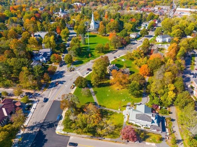 Aerial view of a small town with colorful fall trees, a church with a tall steeple, and surrounding houses and streets.