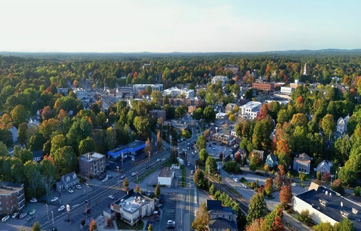 Aerial view of a town with a mix of residential and commercial buildings surrounded by green and fall-colored trees.