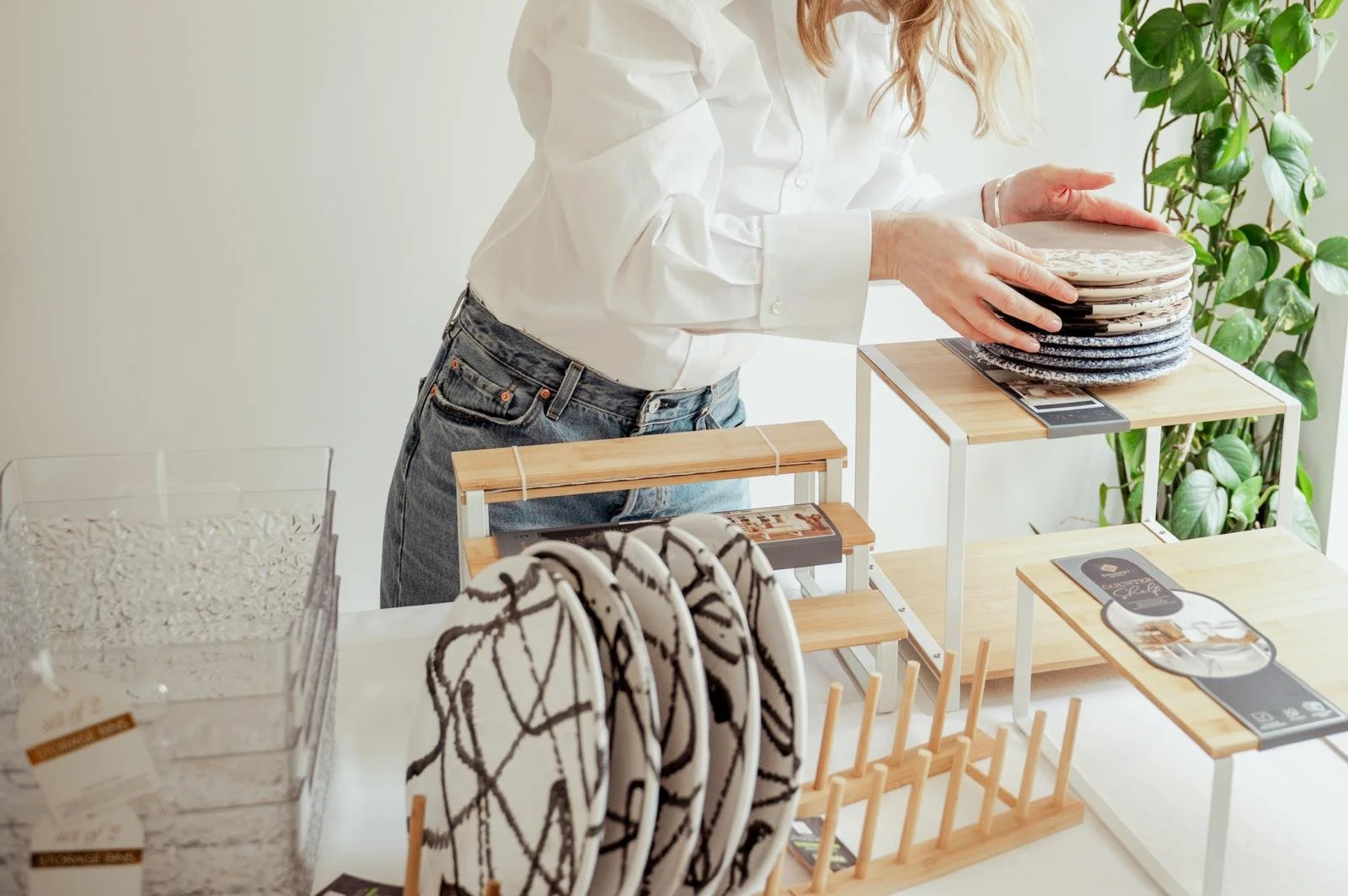 Person holding a ceramic plate at a table with various ceramic dishes and small wooden shelves.