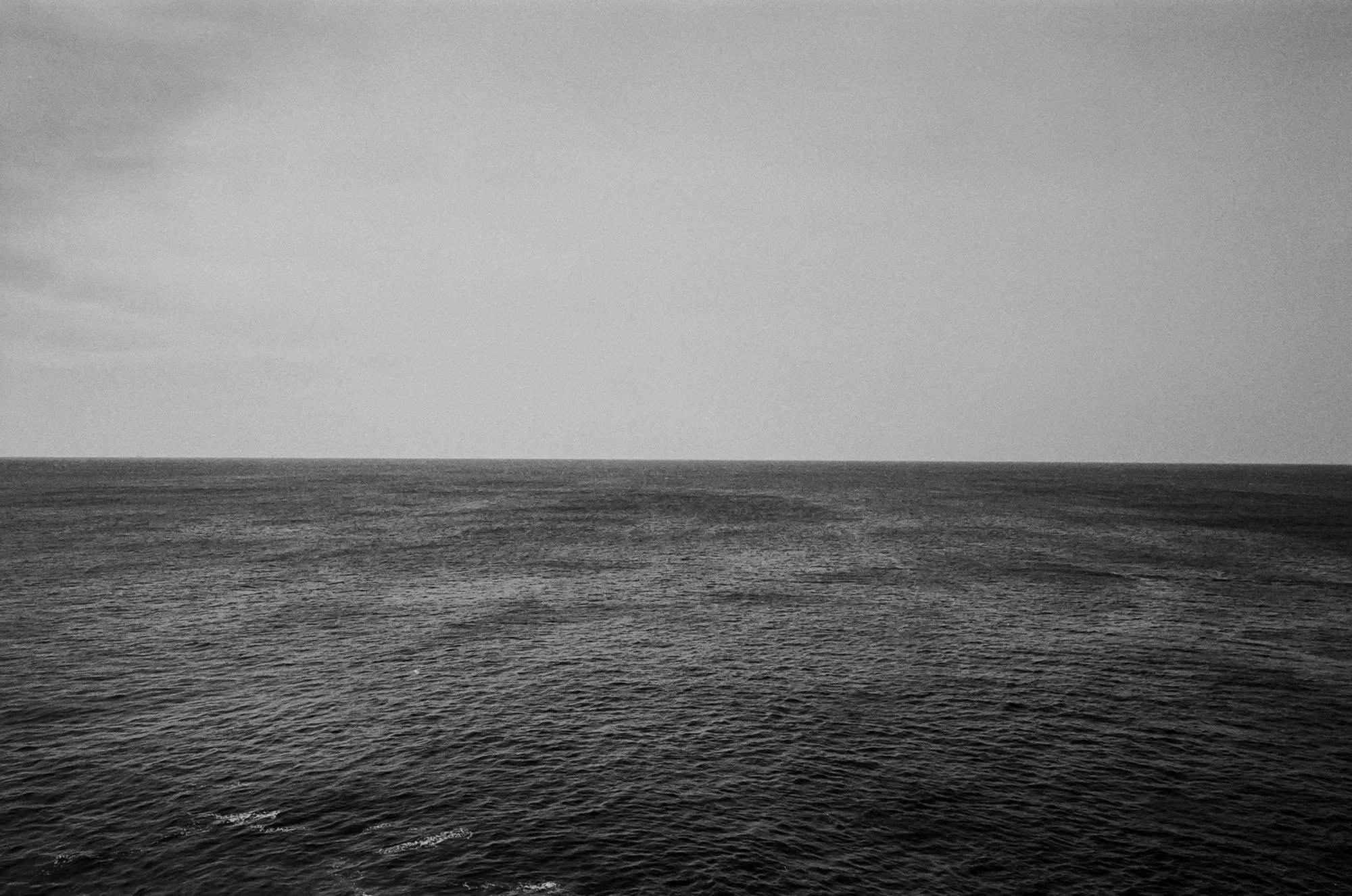 Black and white photo of an ocean horizon with calm water and a cloudy sky.