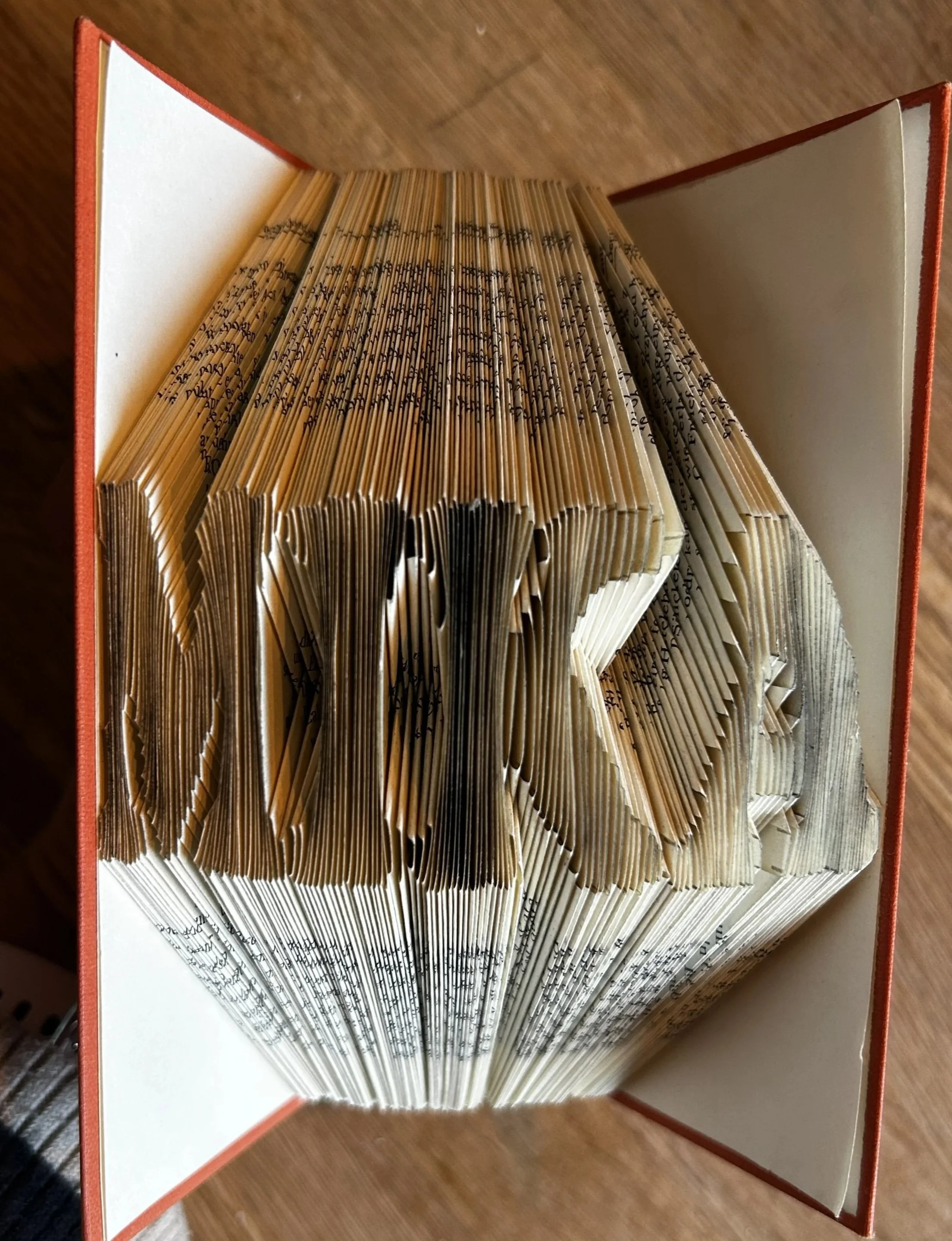 Offener Buch mit gebundenen Seiten, die vom Buchrücken nach außen gebogen sind, auf einem Holzoberfläche liegend.
