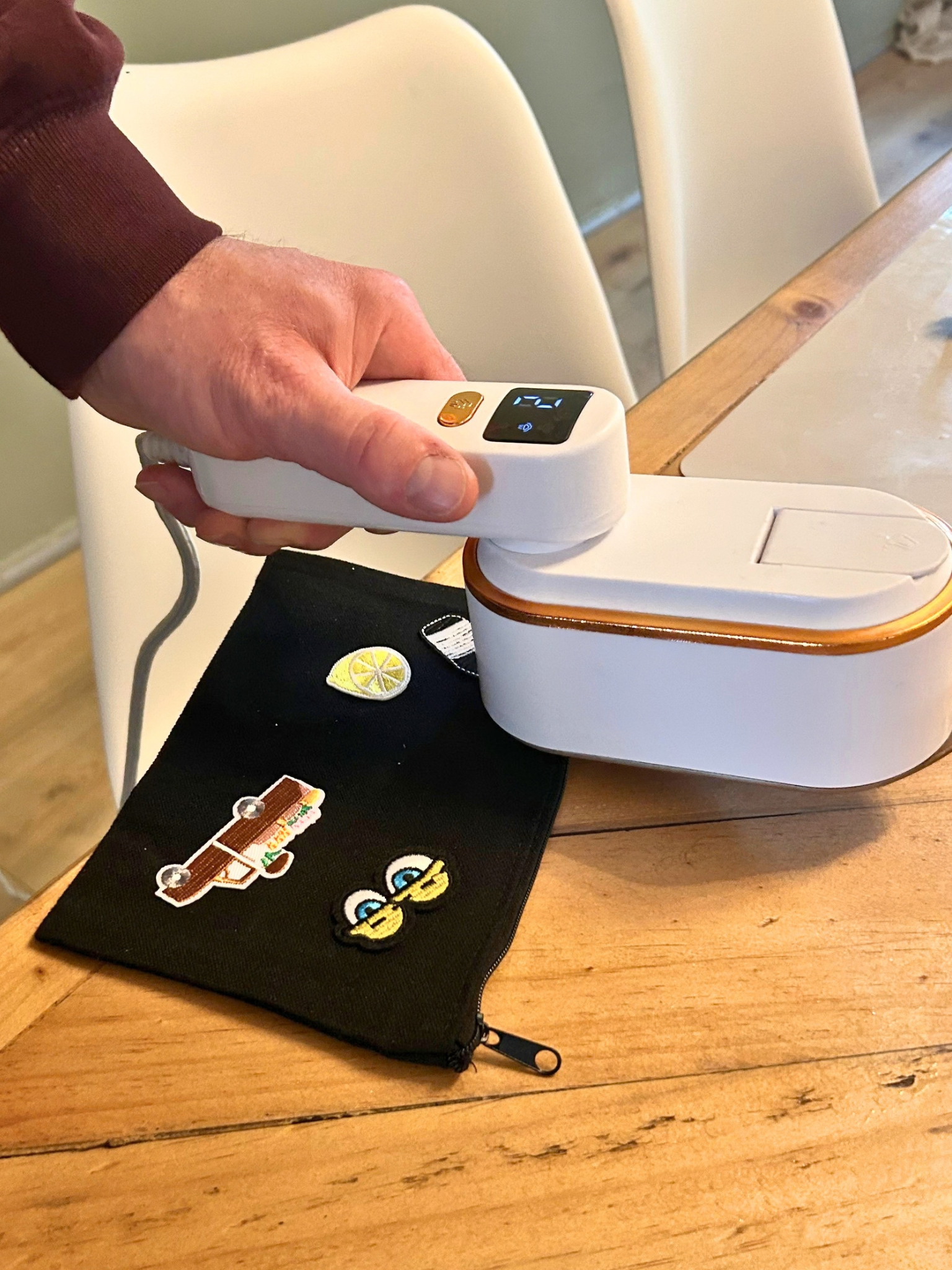 Hand hält ein modernes, digitales Handgerät über einem weißen Kuchen mit orangefarbenem Rand, auf einem Tisch. Im Hintergrund sind weiße Stühle und eine grüne Wand.