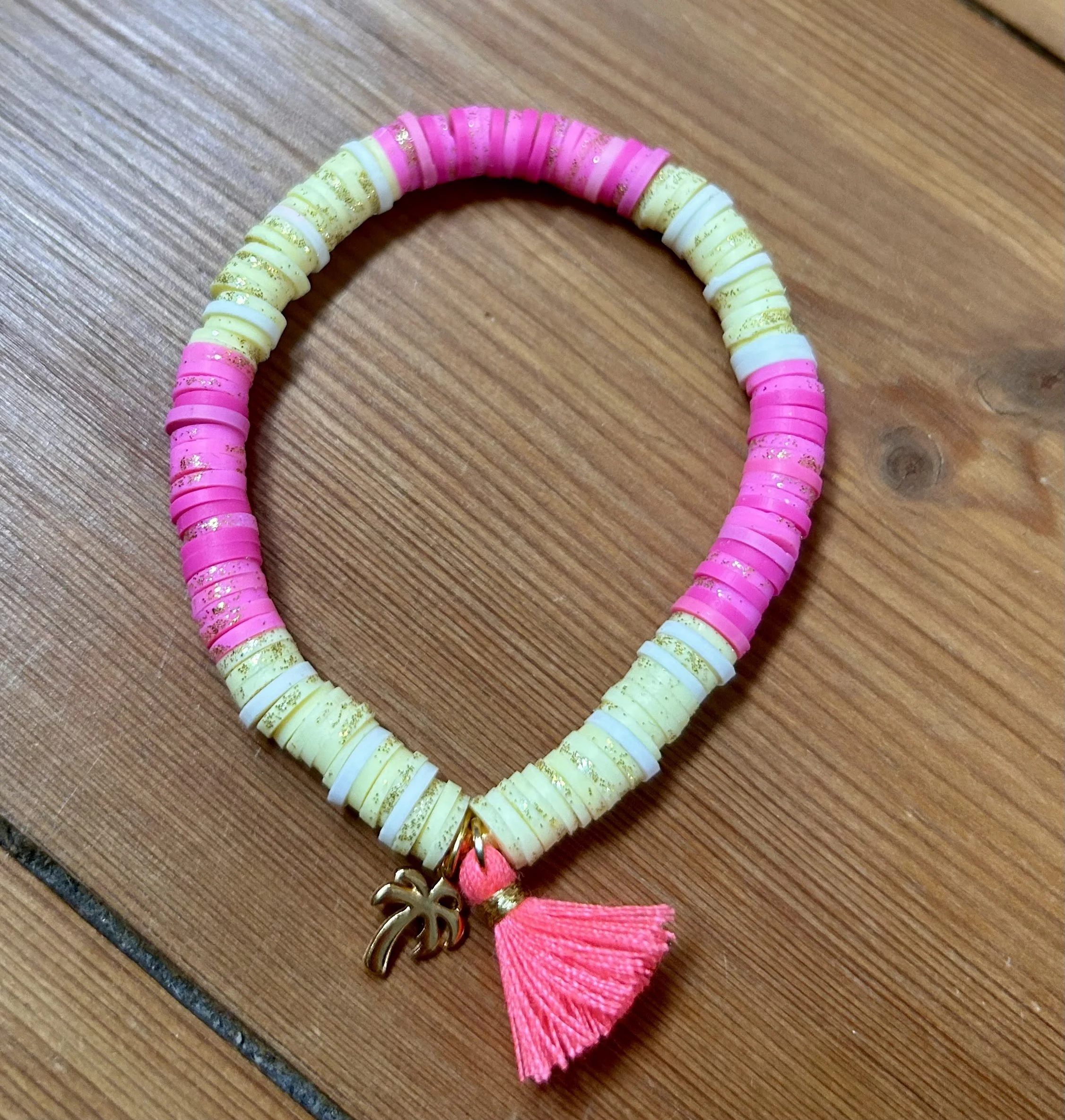 Halskette aus bunten Disc-Perlen in pink, weiß und gelb mit Goldmuster und einem goldfarbenen Anhänger in Form eines Palmenblattes sowie einem pinken Tasschen
