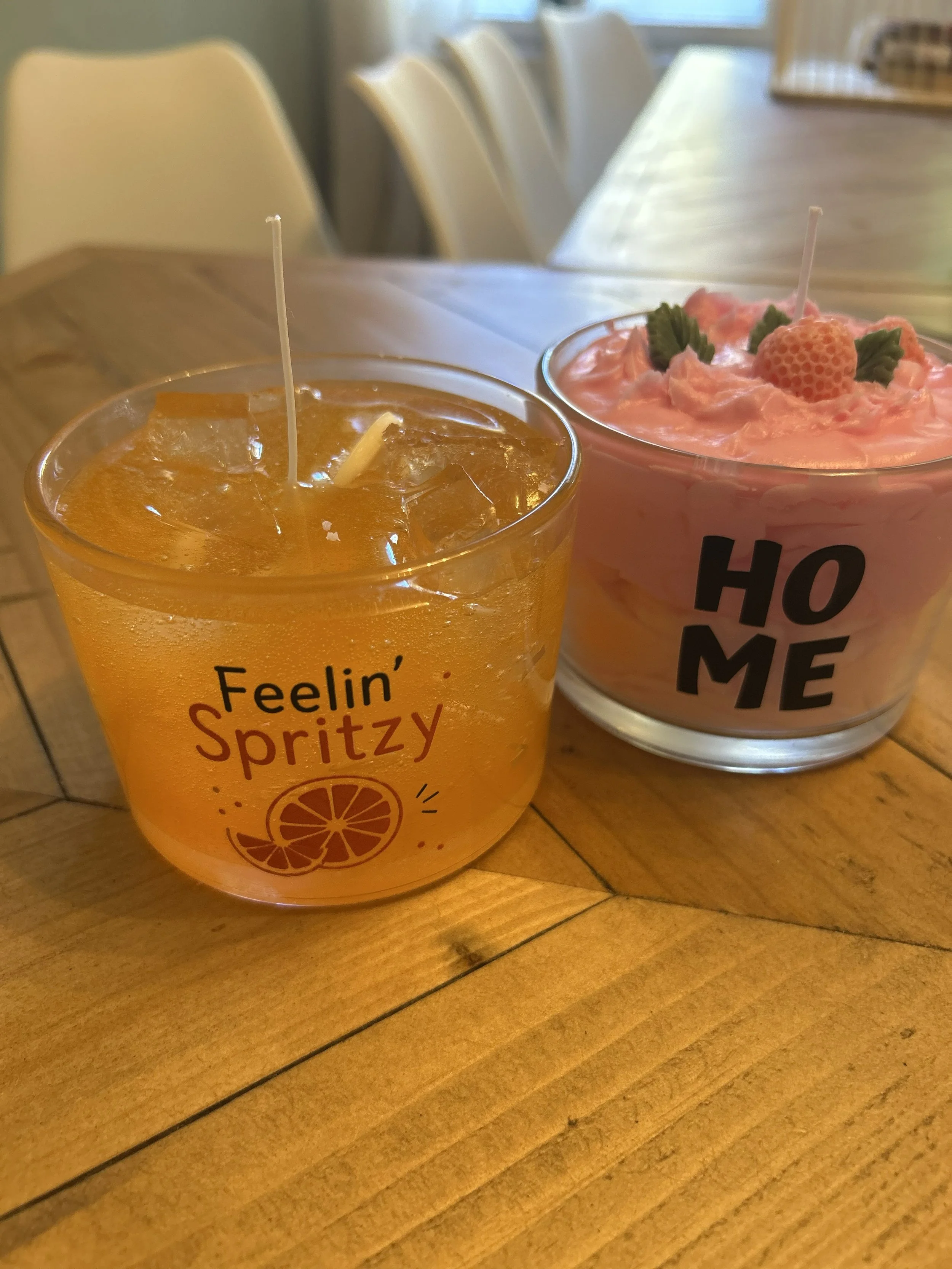 Zwei Gläser mit roten Getränken, verziert mit Beeren und einer Kerze, auf einem Holztisch. Das vordere Glas hat ein Etikett mit deutschem Text.