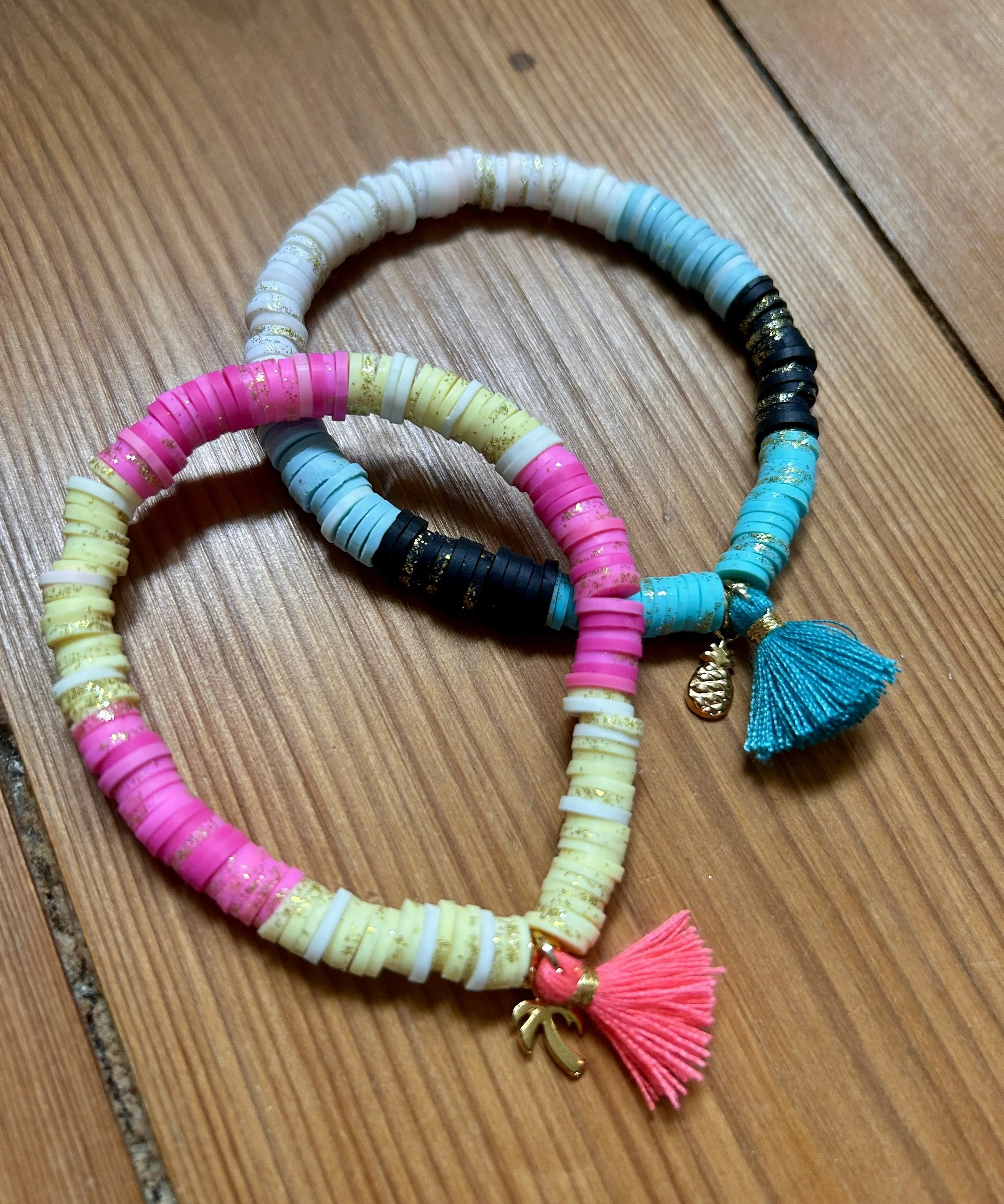 Bunte Armbänder aus kleinen Ton- oder Kunststoffperlen mit Anhängern und Quasten, auf einem Holztisch.