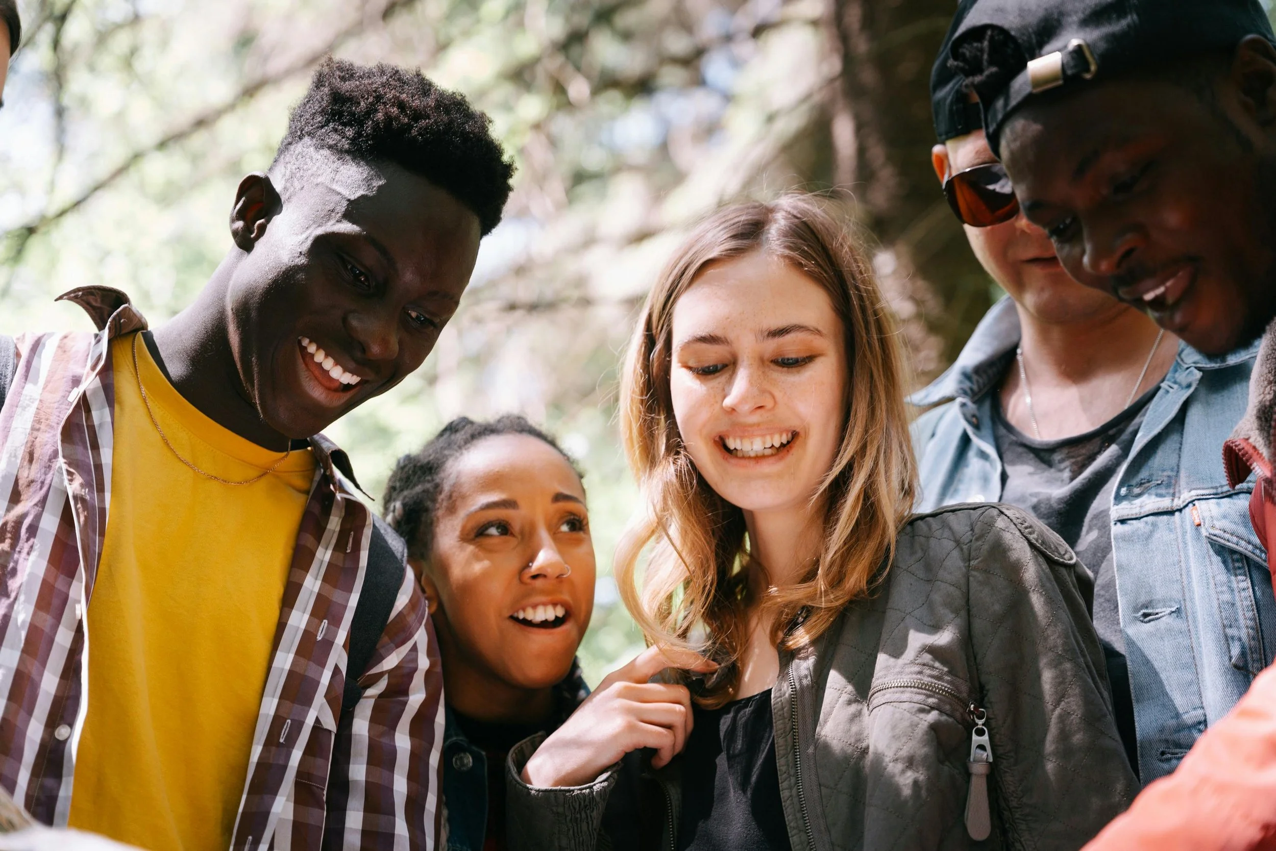 A diverse group of young people looking at a phone outdoors in a wooded area. Brightmane Therapeutic Center San Jose, CA